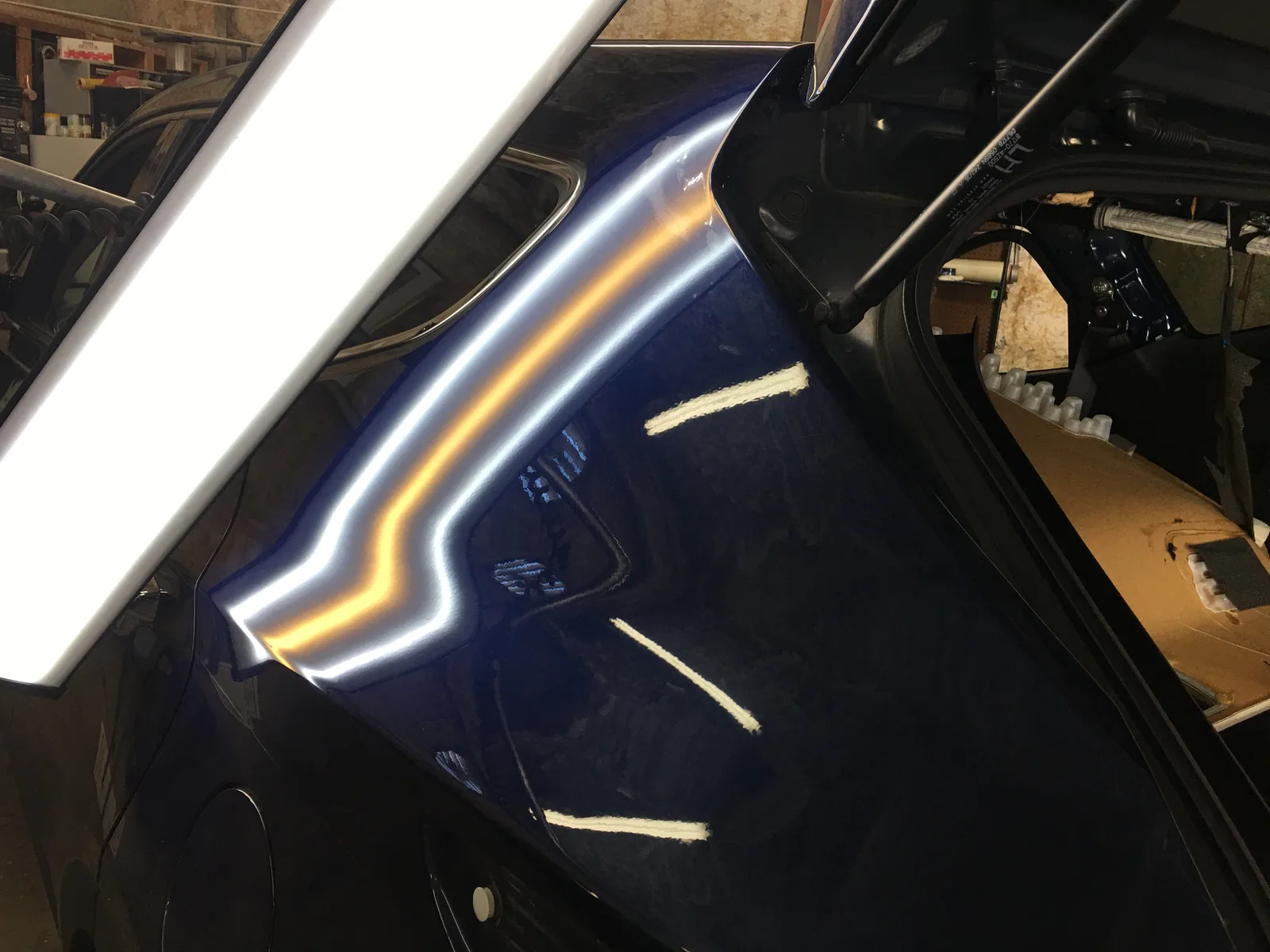 Dark blue quarter panel after crease repair, the PDR light bar reflection running straight across it
