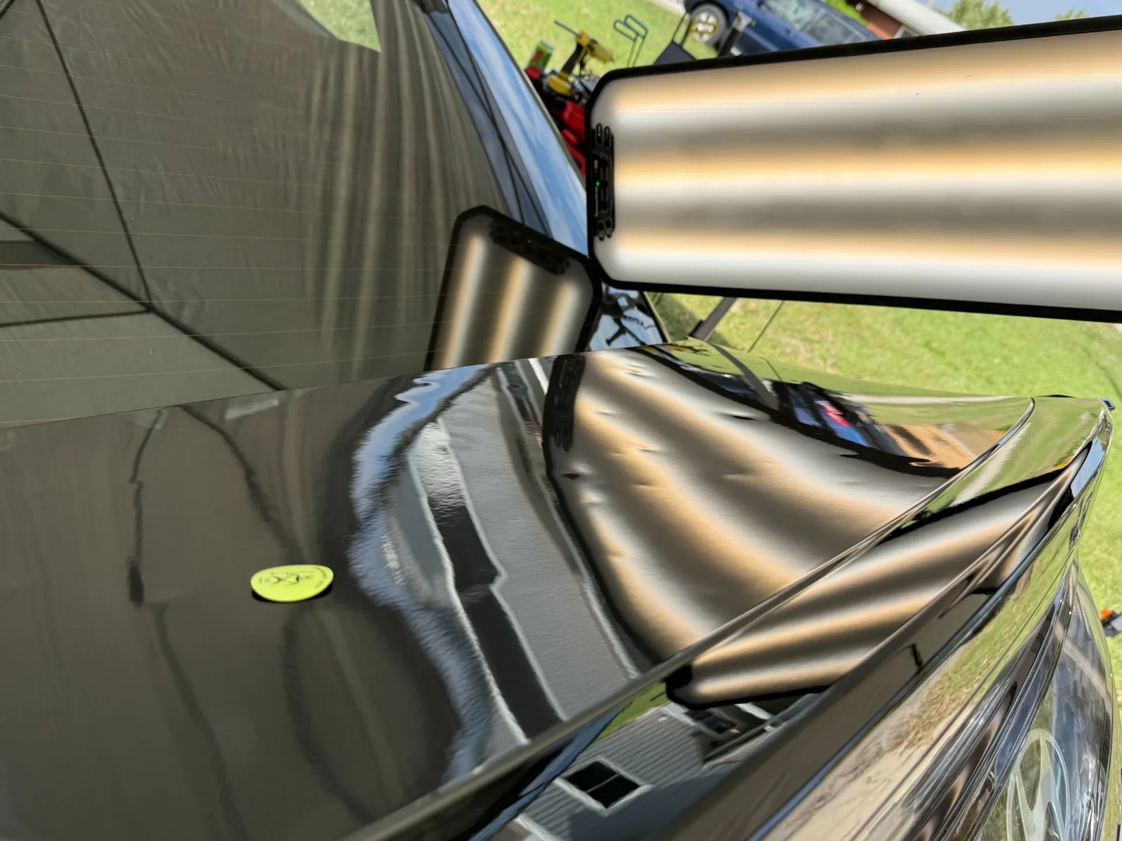 Black hood and fender under a PDR light bar, the reflection revealing hail dents during inspection