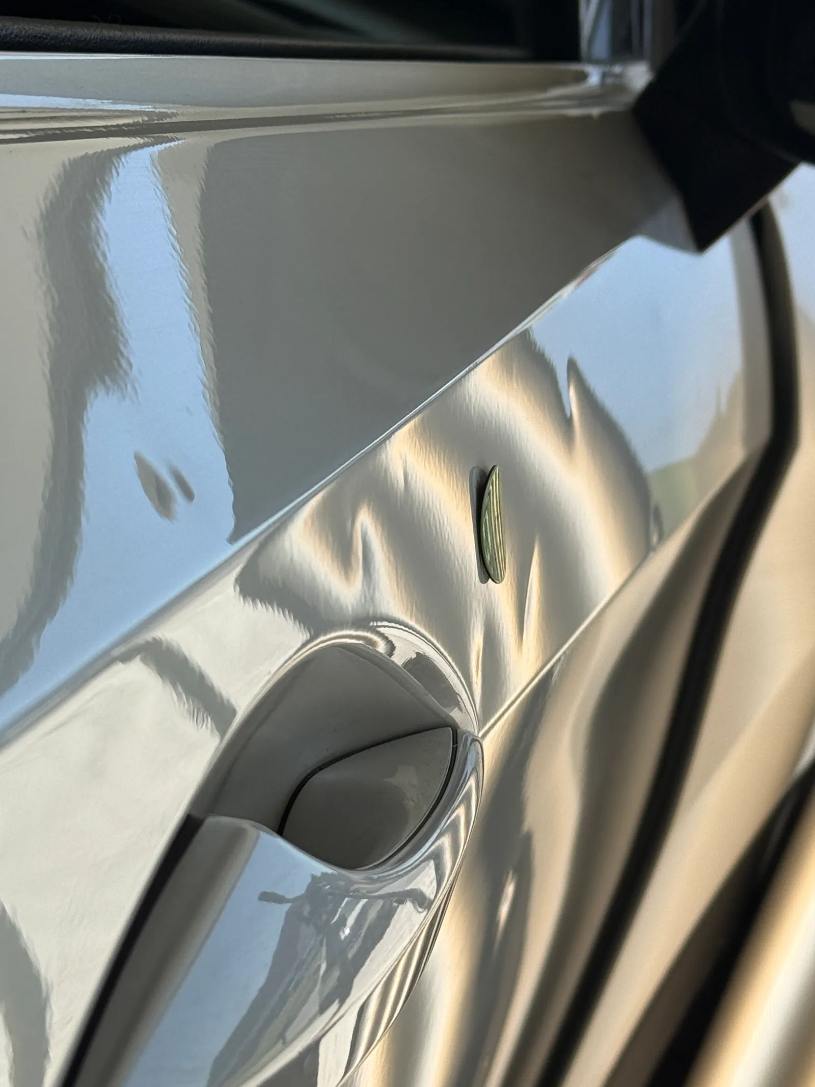 Coin placed next to hail dents on a silver fender near the mirror mount and body line