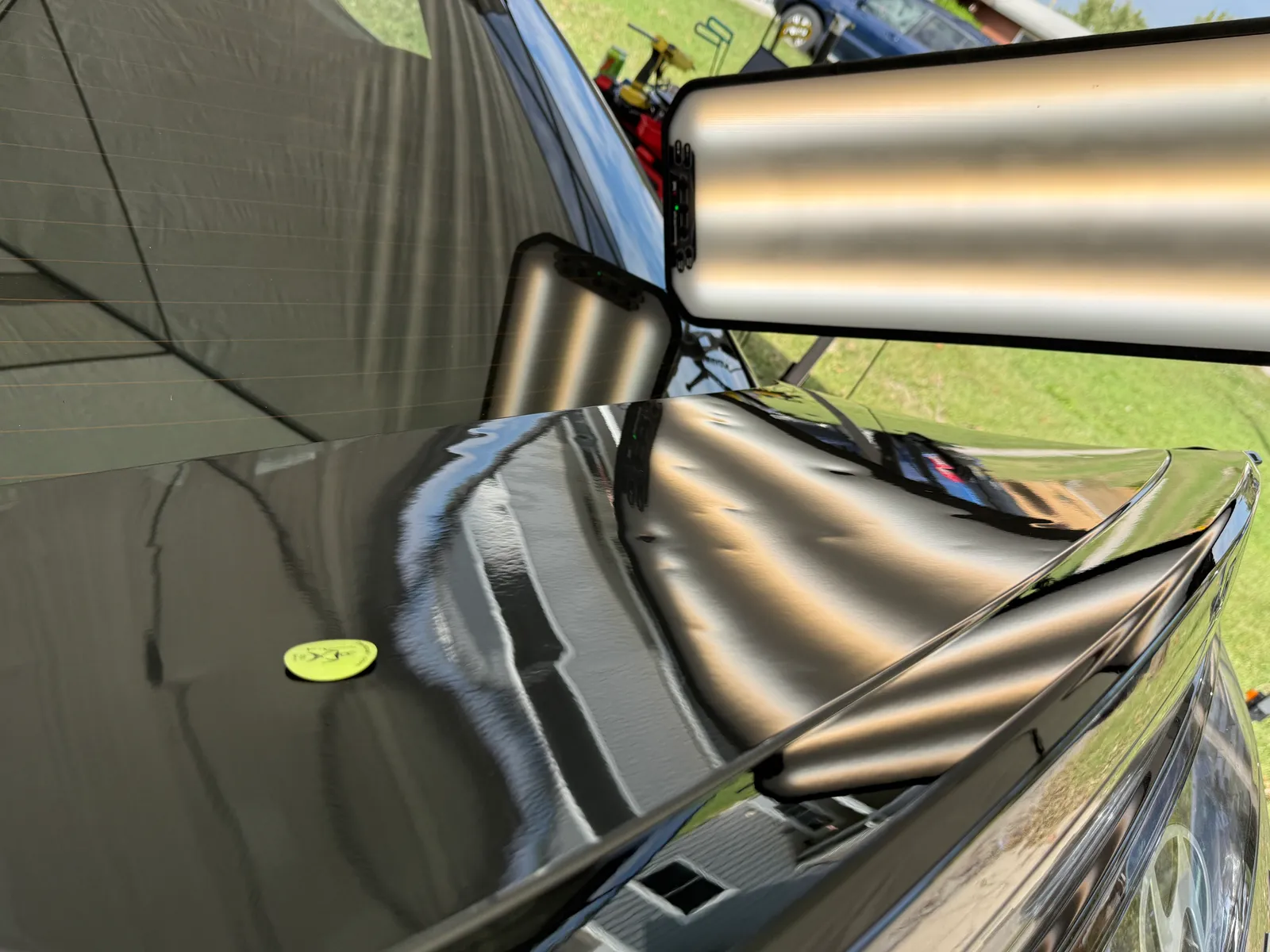 Green PDR gauge chip on a black hood with hail dents revealed by a light bar reflection
