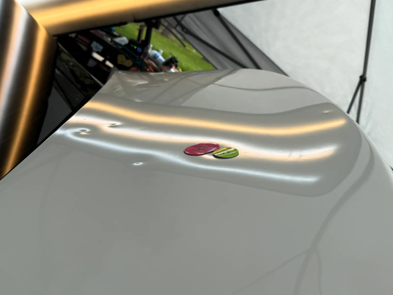 Two coloured PDR gauge chips laid on a white hood beside hail dents for size reference