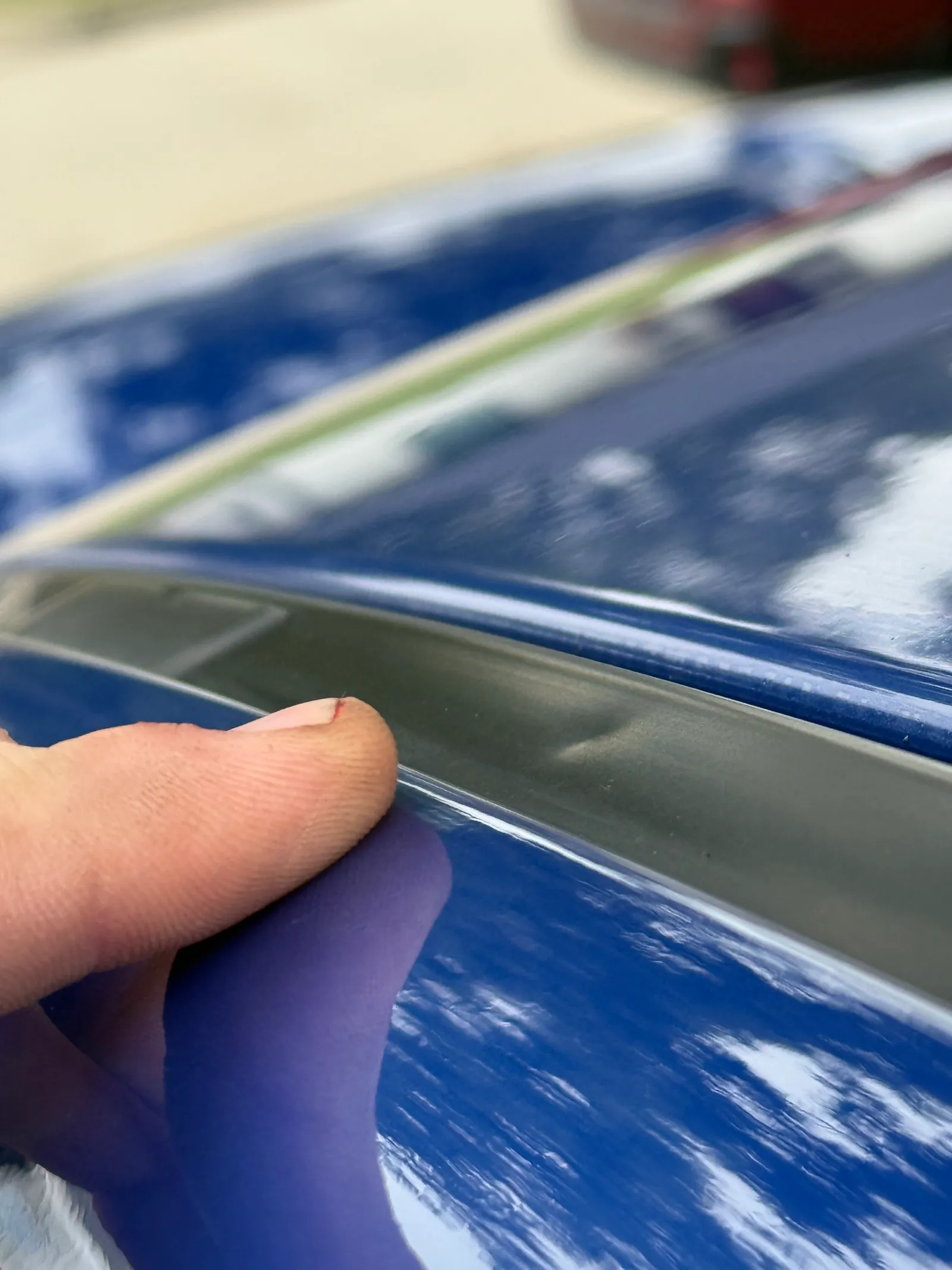 Gloved hand feeling along the roof rail edge of a blue vehicle to check for hail damage