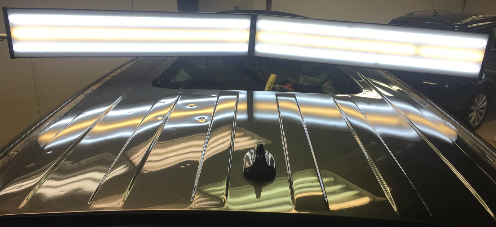 Roof panel under dual PDR light bars — hail dents still visible on one half, repaired on the other