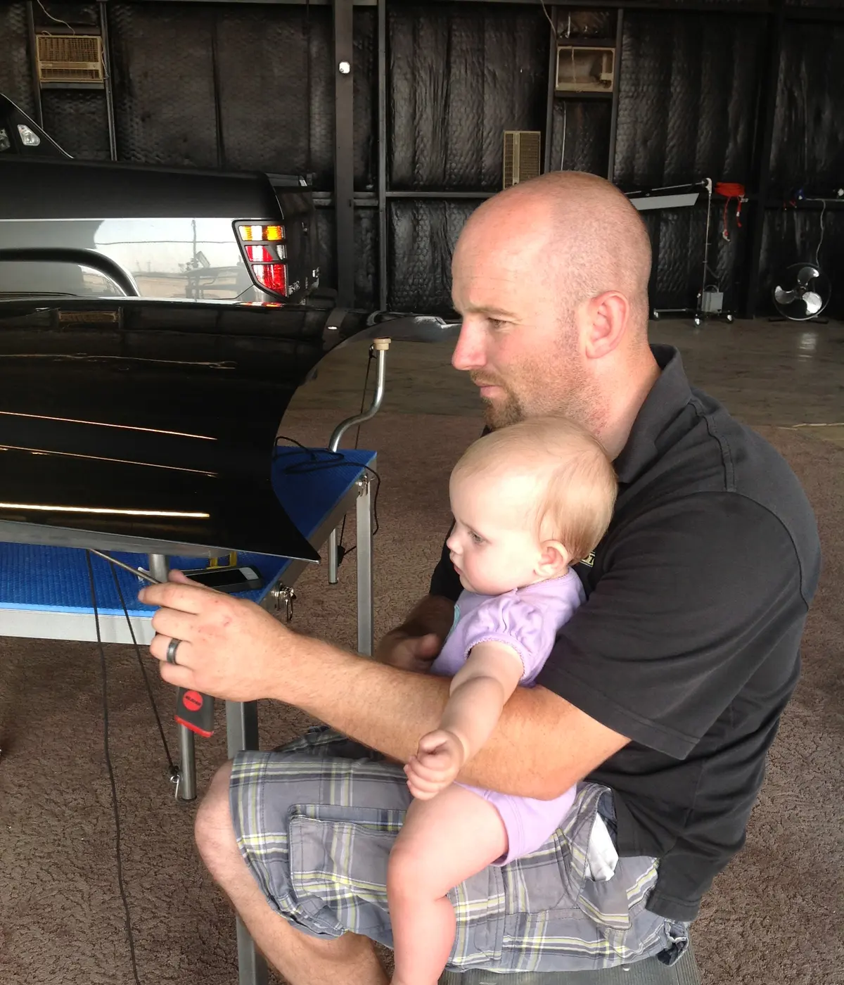 Jeremy, founder of Hail Depot, working a dent with a PDR rod while holding his daughter in his lap